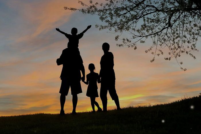 A silhouette of a family standing on top of a hill at sunset.