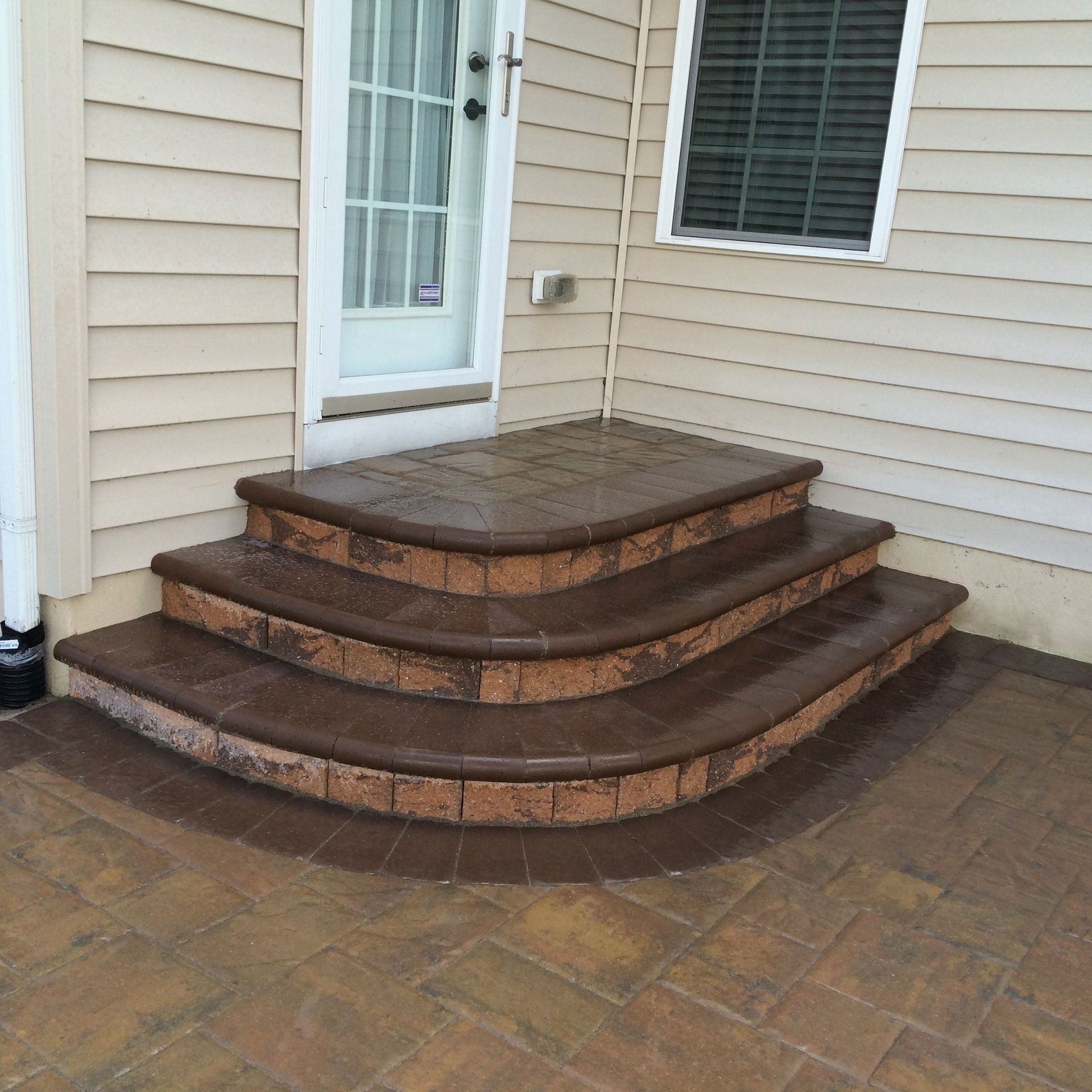 Three curved stone steps leading to a white door against beige vinyl siding on a patio.