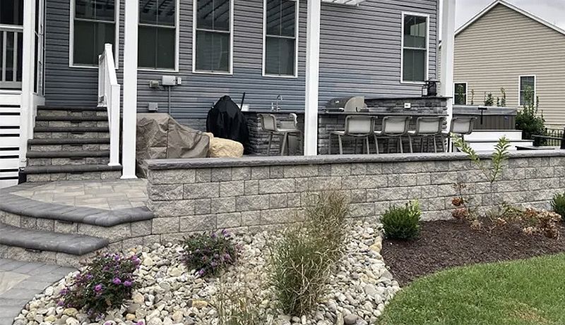 A house with a patio and a stone wall in front of it.