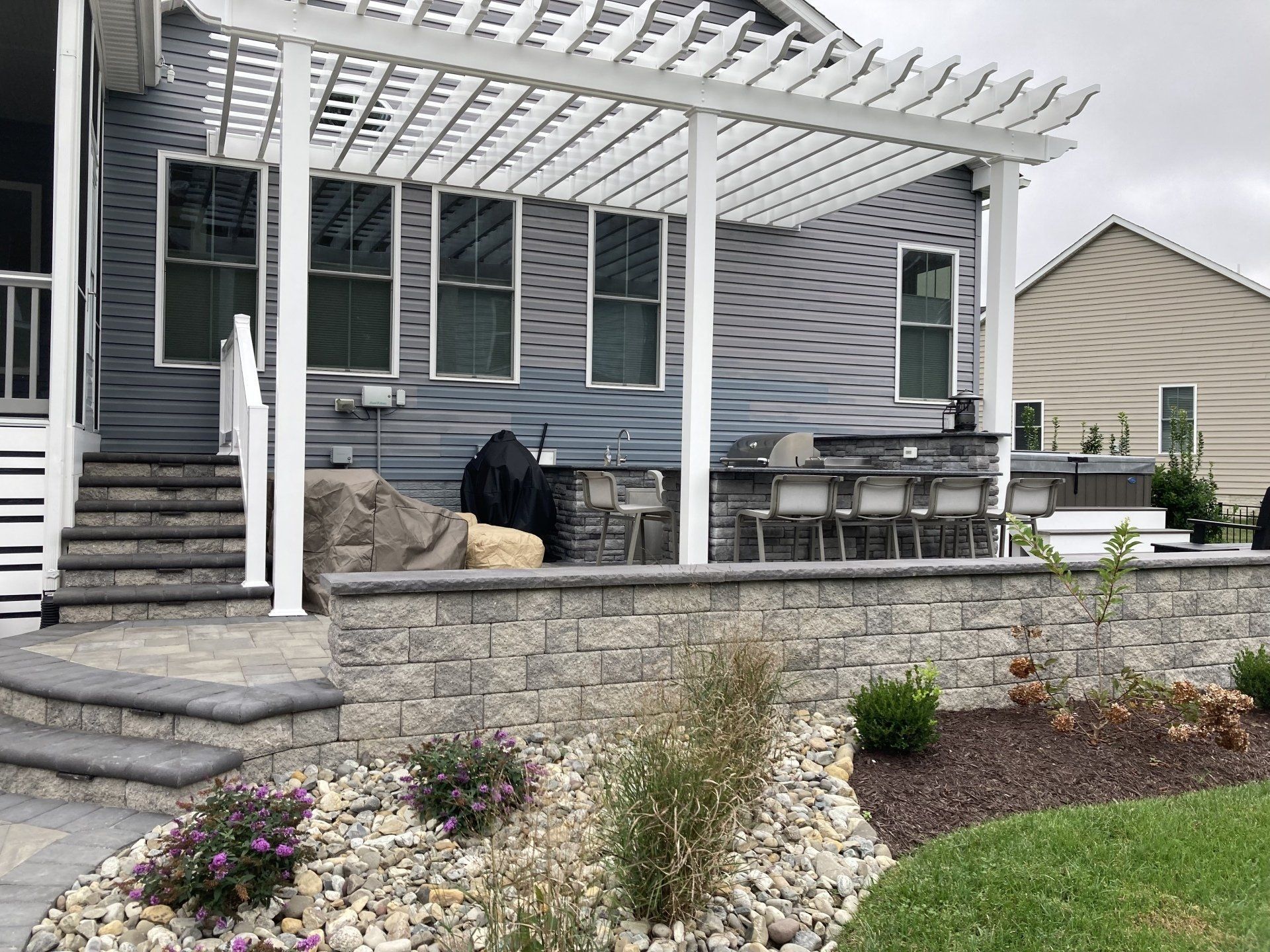 The backyard of a house with a pergola and a grill.