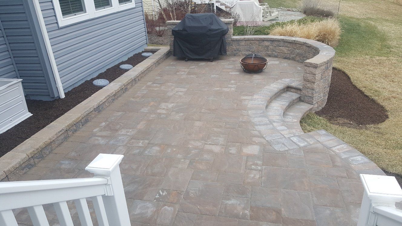 A patio with a grill and a fire pit in front of a house.