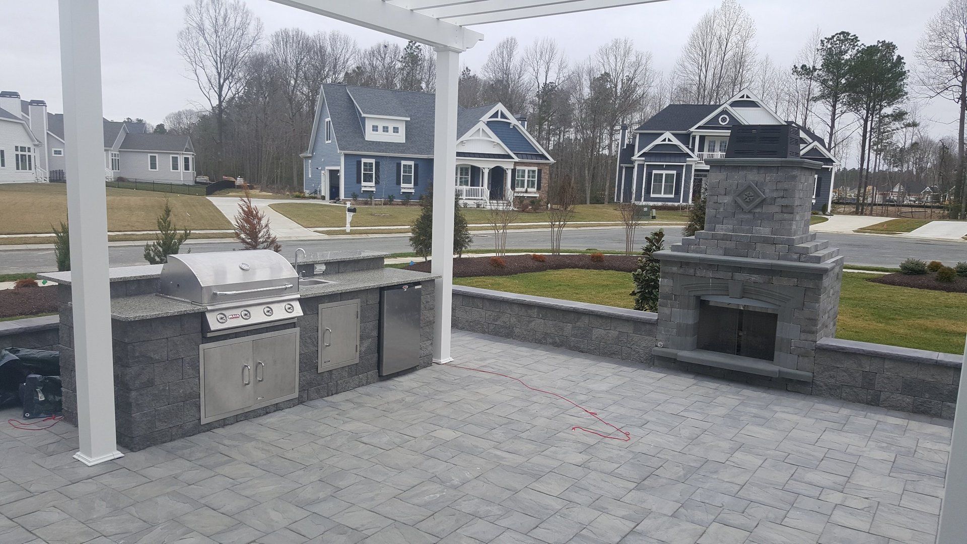 A patio with a grill and a fireplace in front of a row of houses.