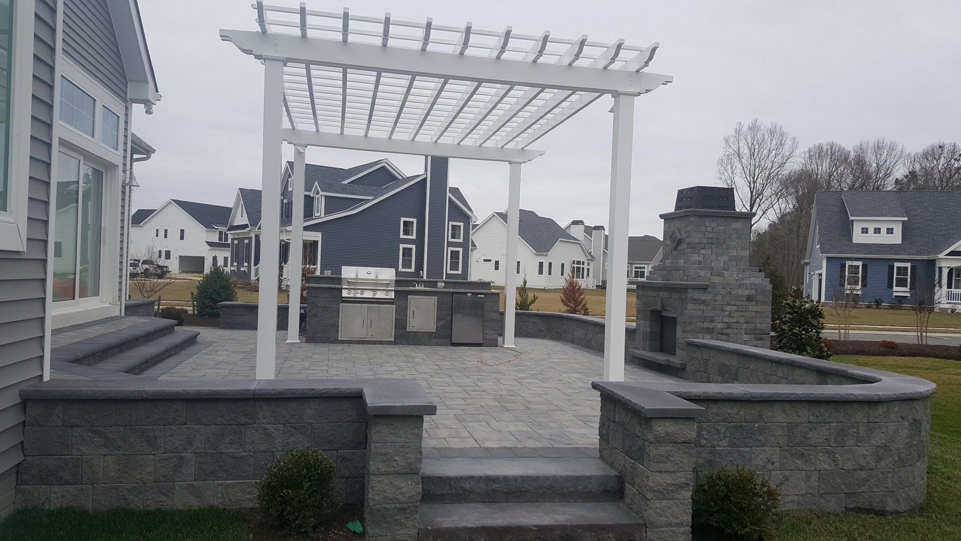 A patio with a pergola and a fireplace in front of a house.