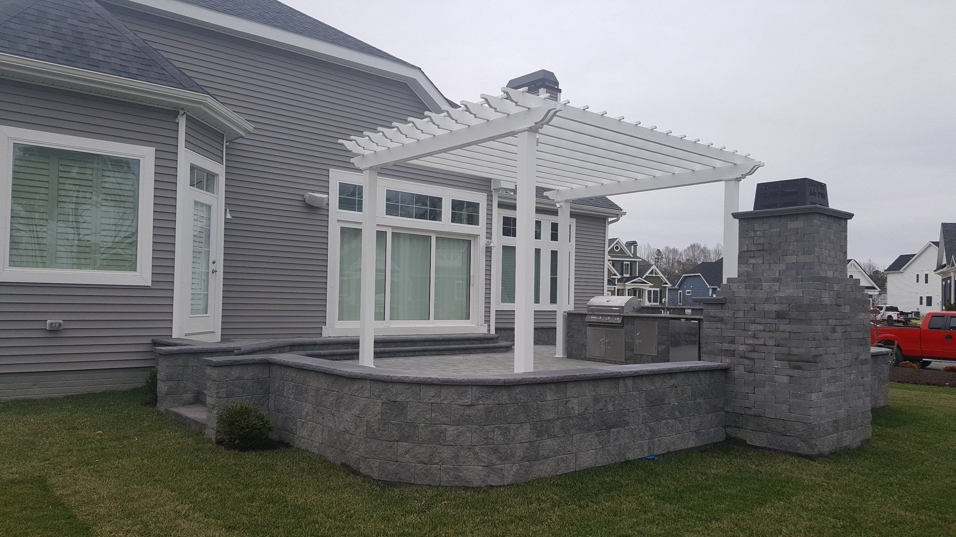 A house with a pergola and a fireplace in front of it.