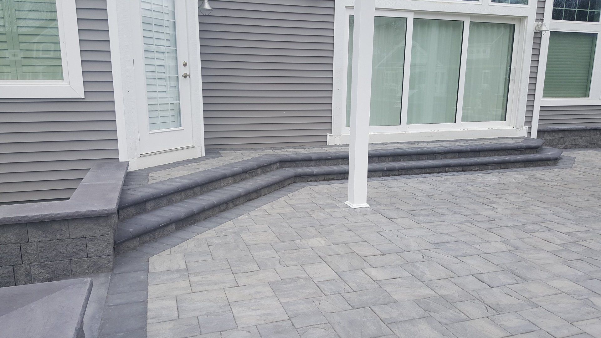 A brick patio in front of a house with stairs leading up to it.