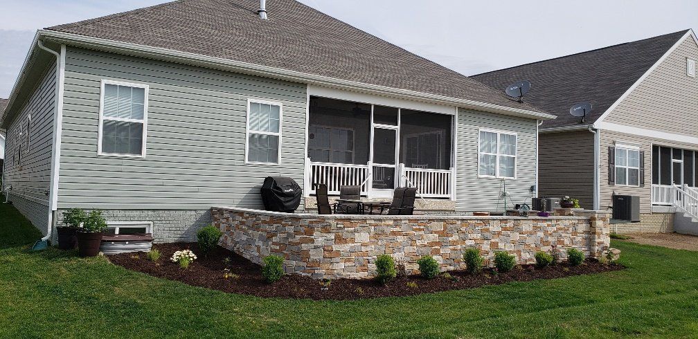 A house with a screened in porch and a stone wall in the backyard.