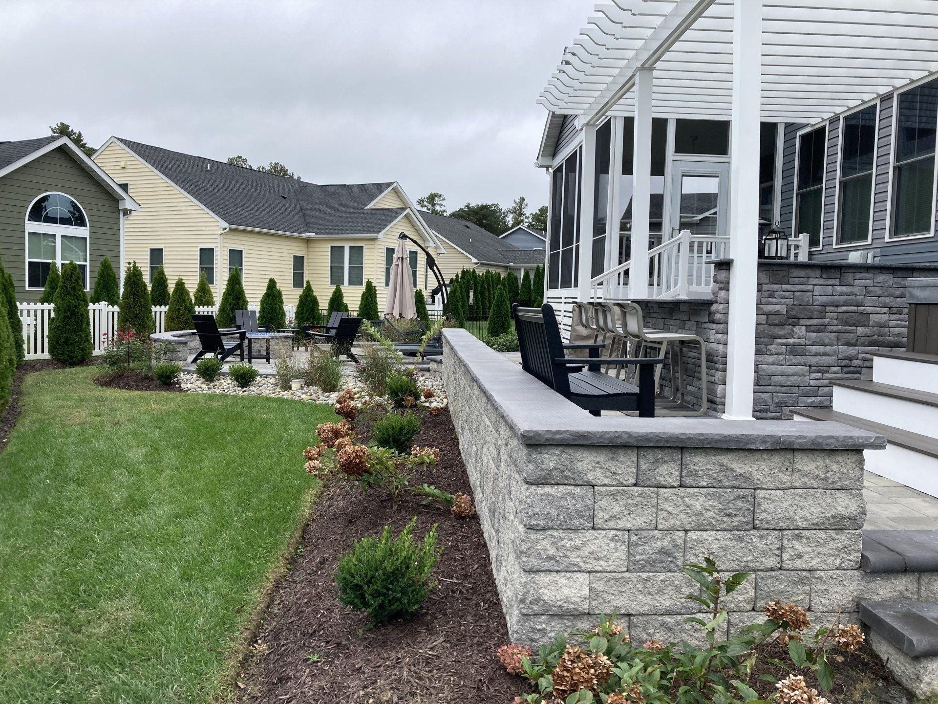 A house with a pergola and chairs in the backyard.