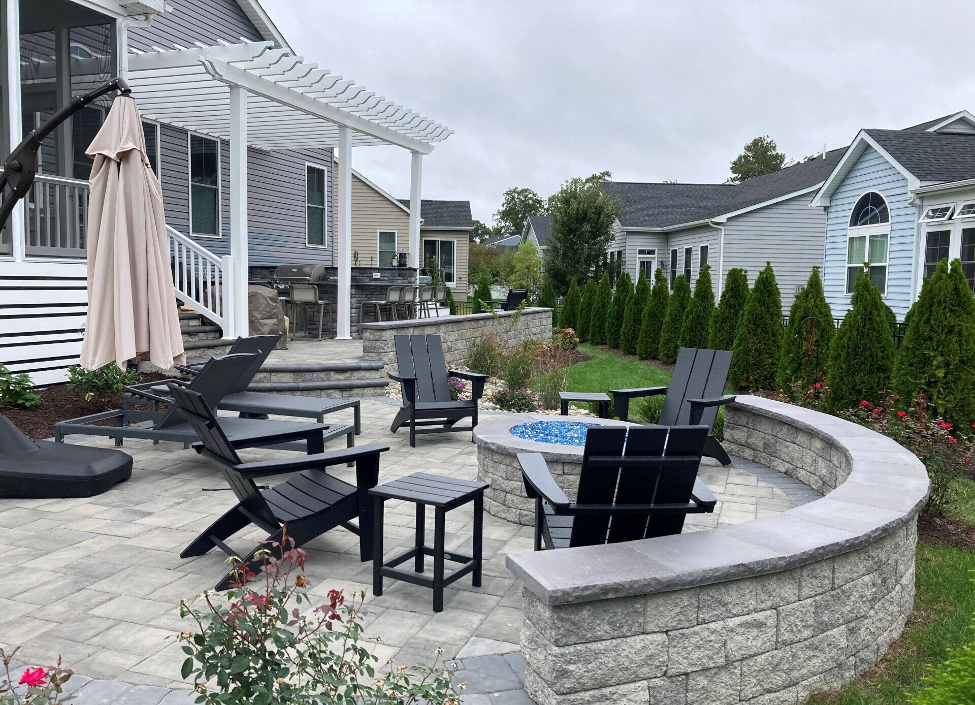 A patio with a fire pit and chairs in front of a house.