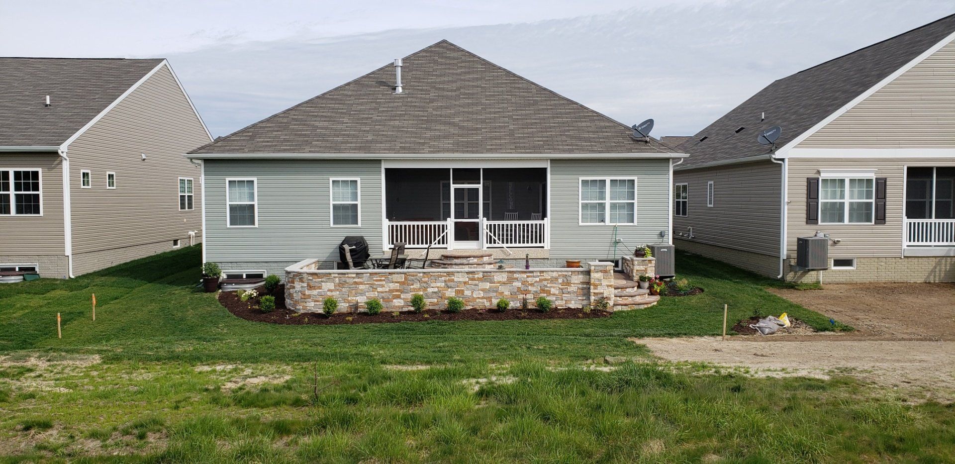 The back of a house with a screened in porch and a stone wall.