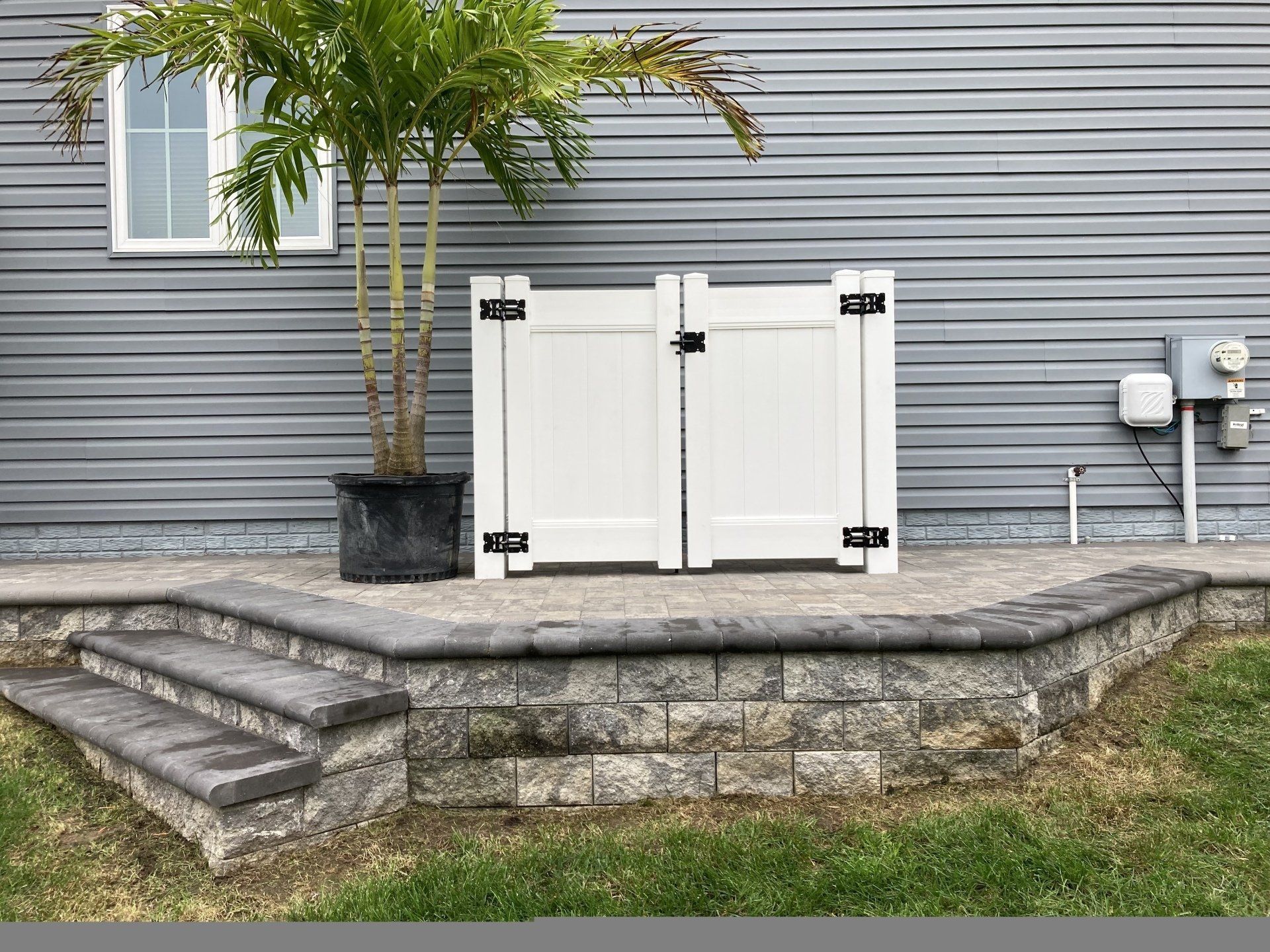 A white fence is sitting on top of a stone wall next to a house.
