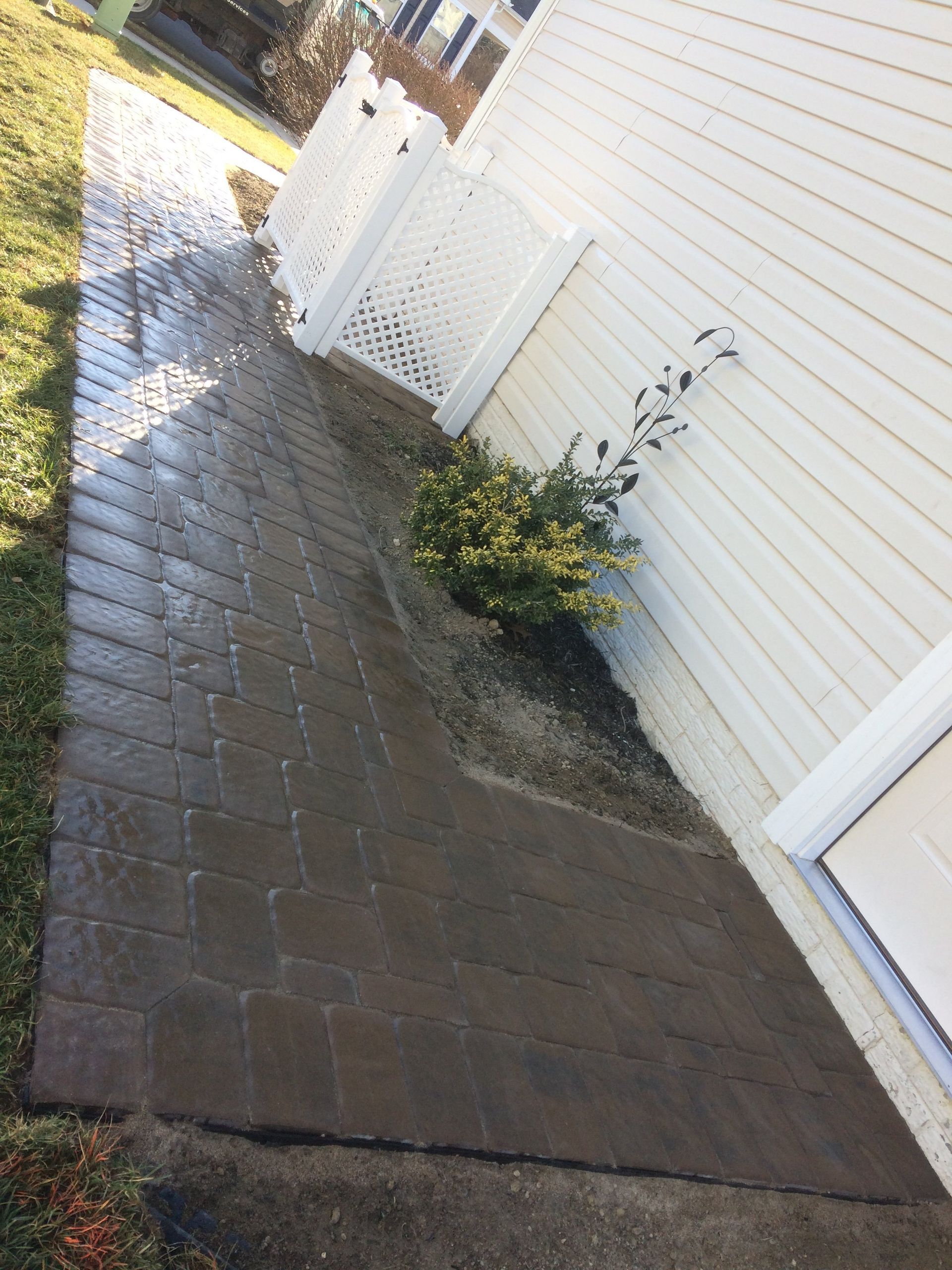 A sidewalk next to a house with a white fence.