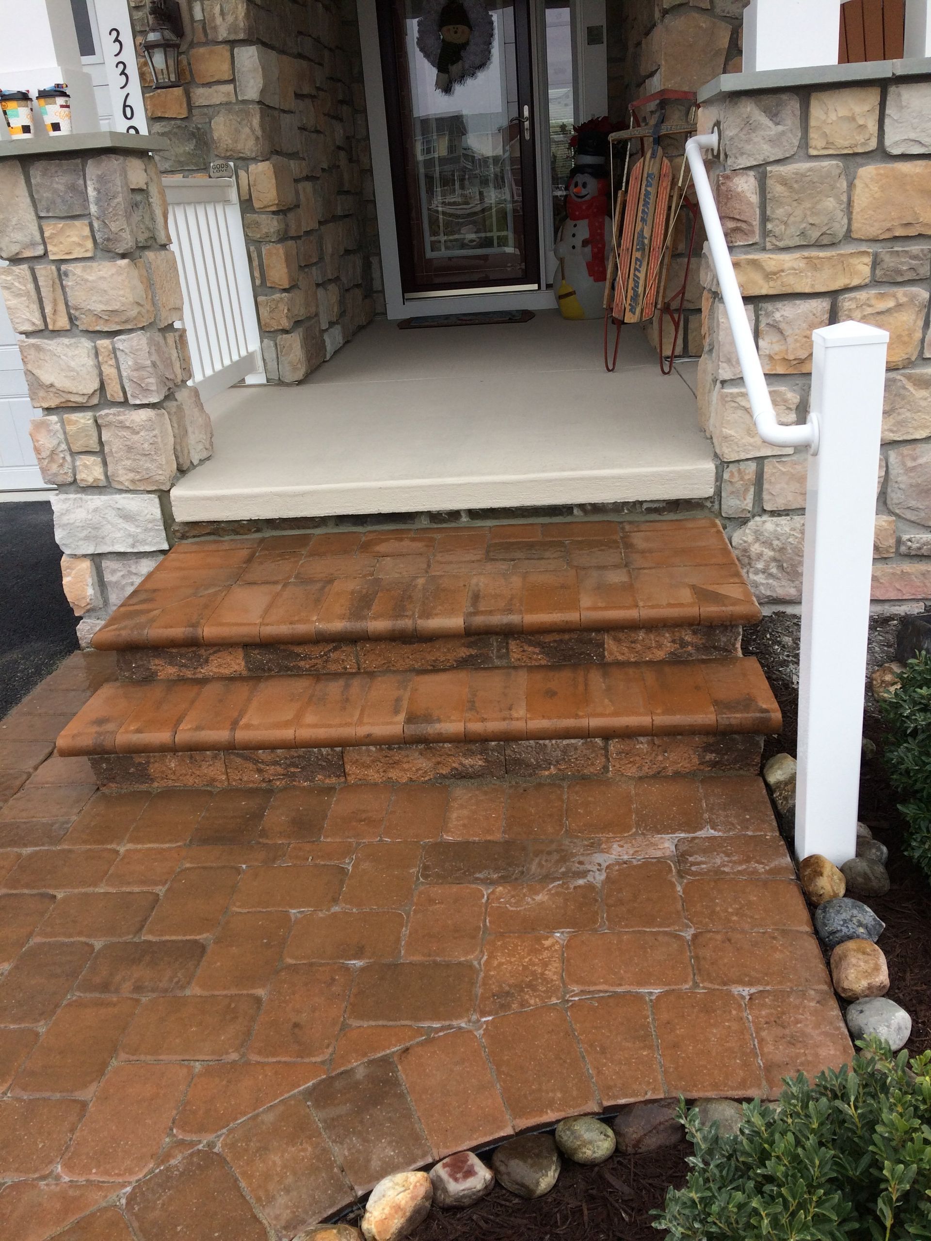A stone porch with brick steps and a white railing.