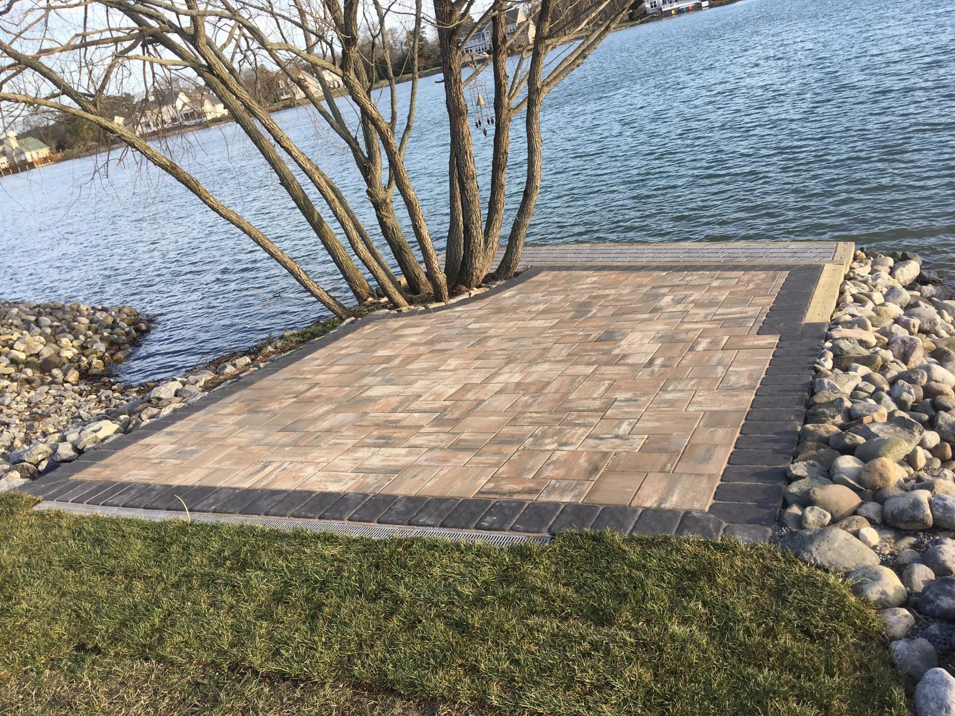 A brick walkway leading to a lake with a tree in the background.