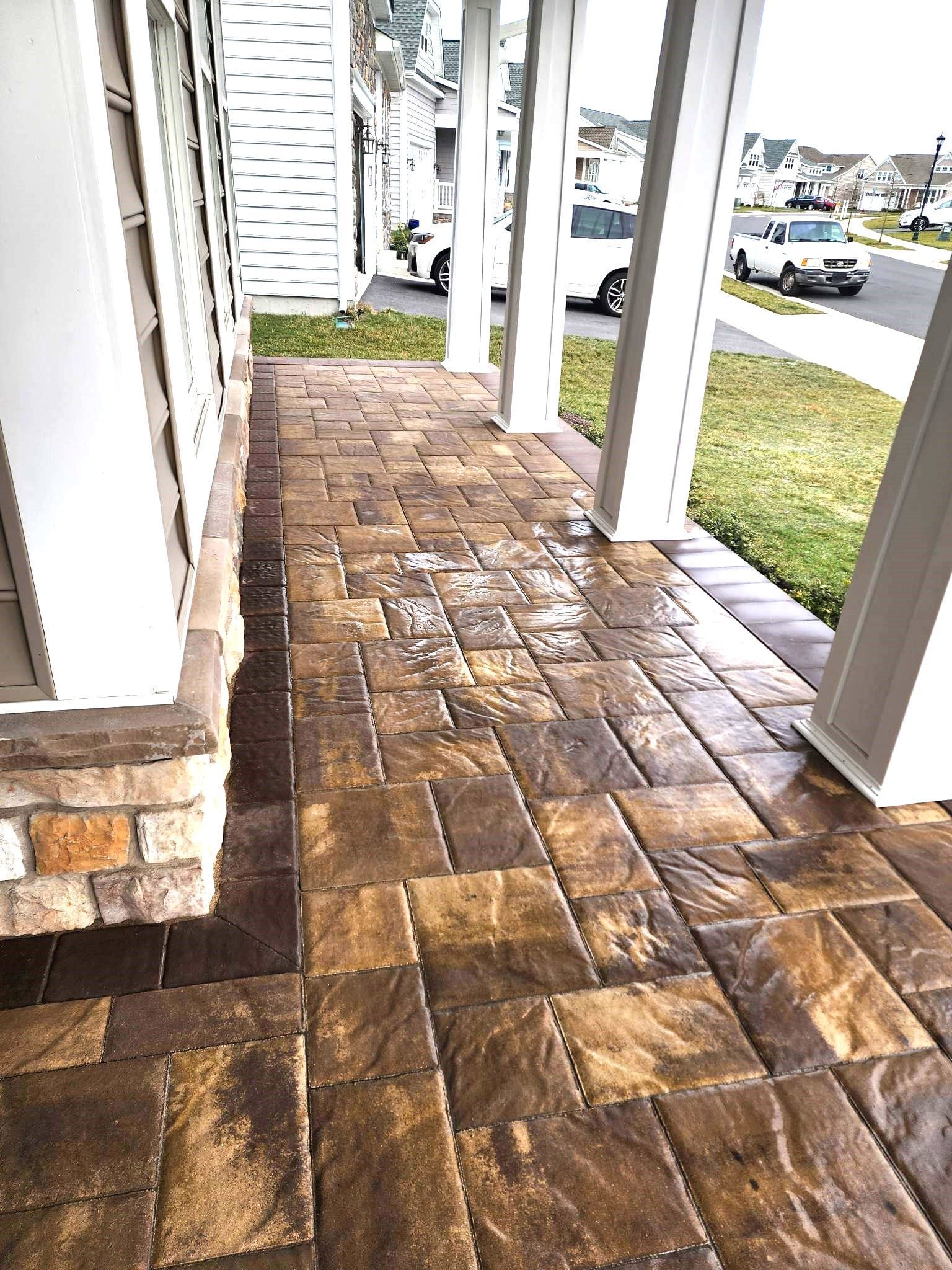 A brick walkway leading to a house with a car parked in the background.