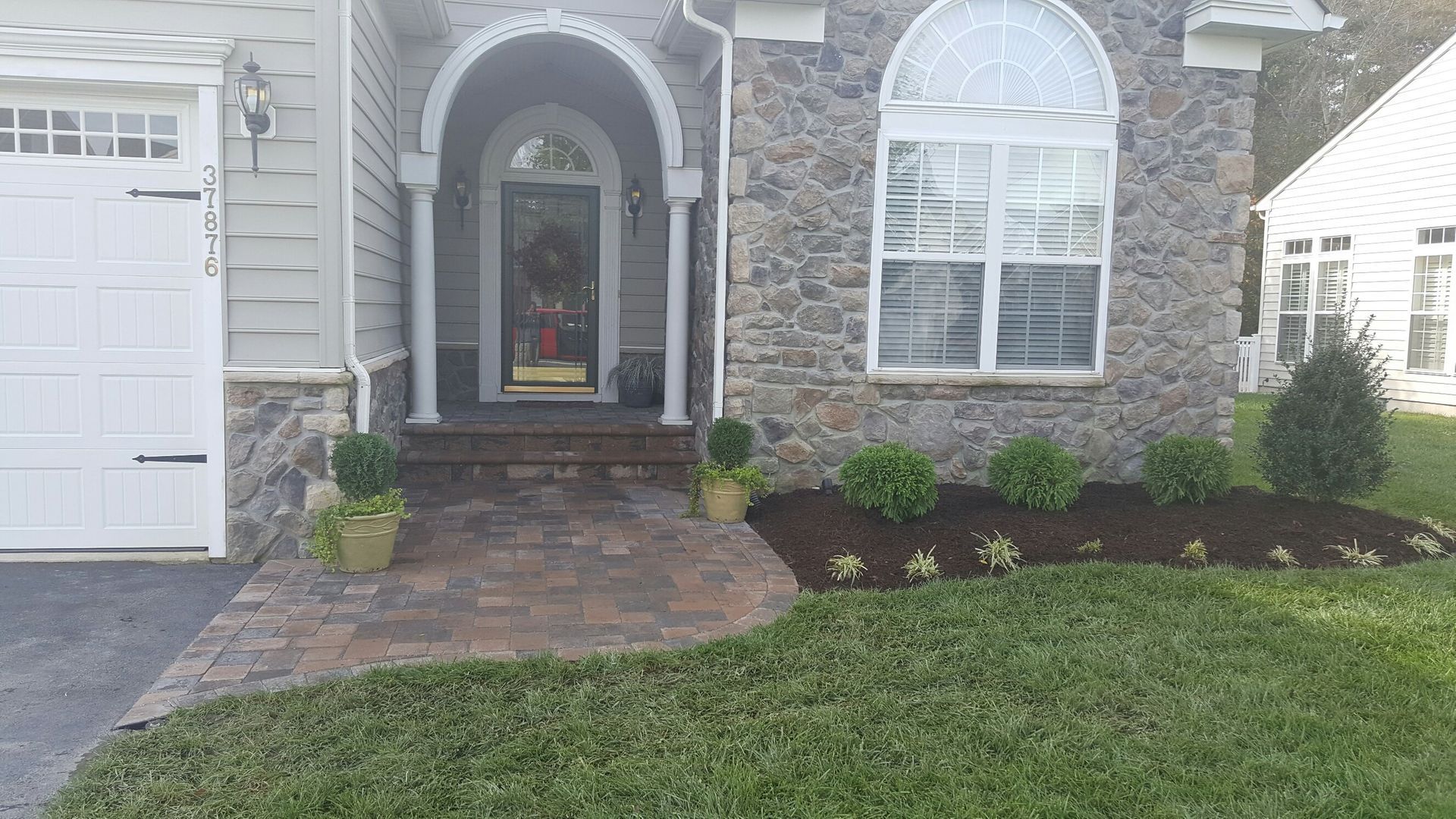 A stone house with a white garage door and a brick walkway leading to the front door.