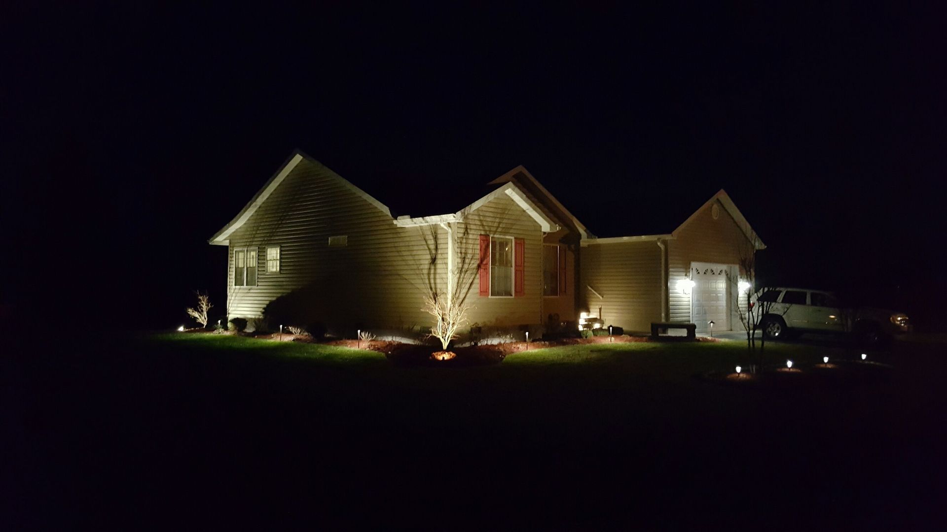 A house is lit up at night with a car parked in front of it.