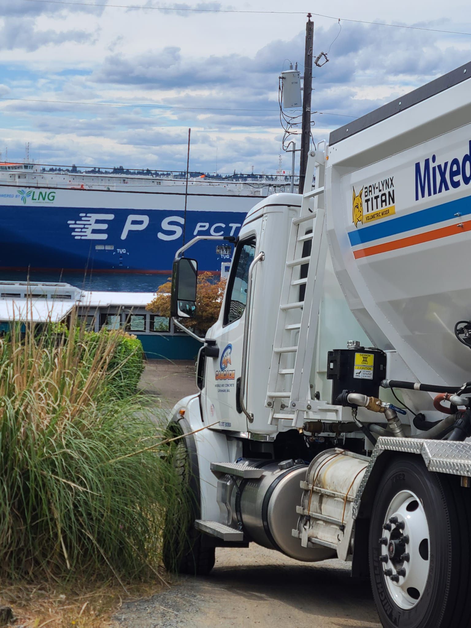 A mixed fuel truck is parked in front of a large ship.