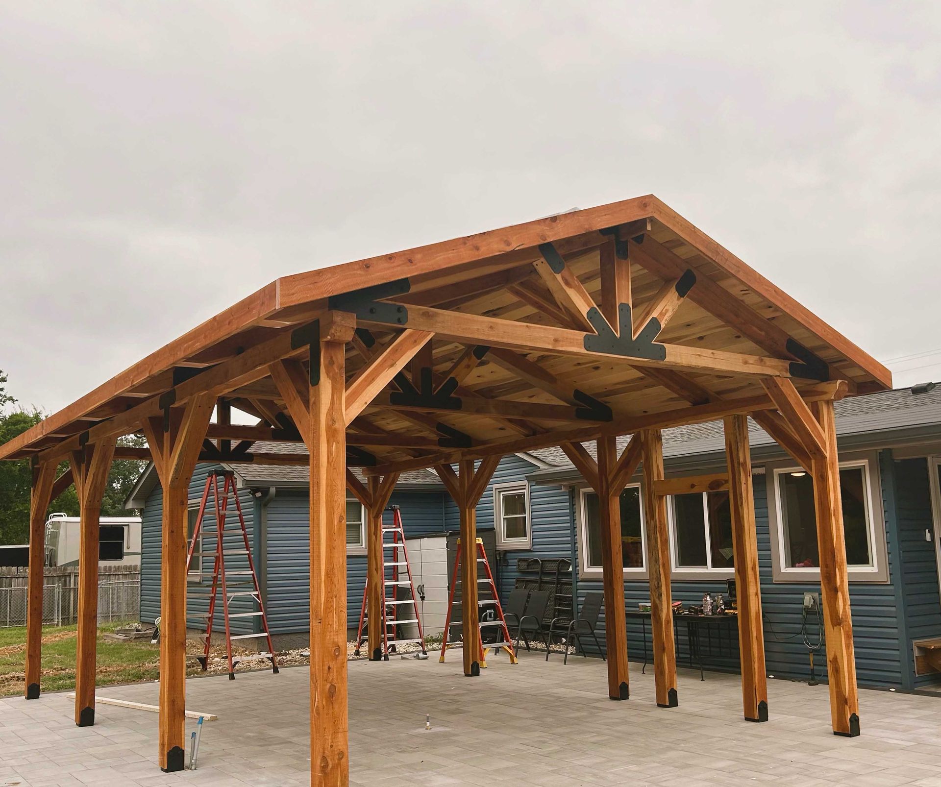 Wooden carport under construction; beams, posts, and roof visible against a cloudy sky.