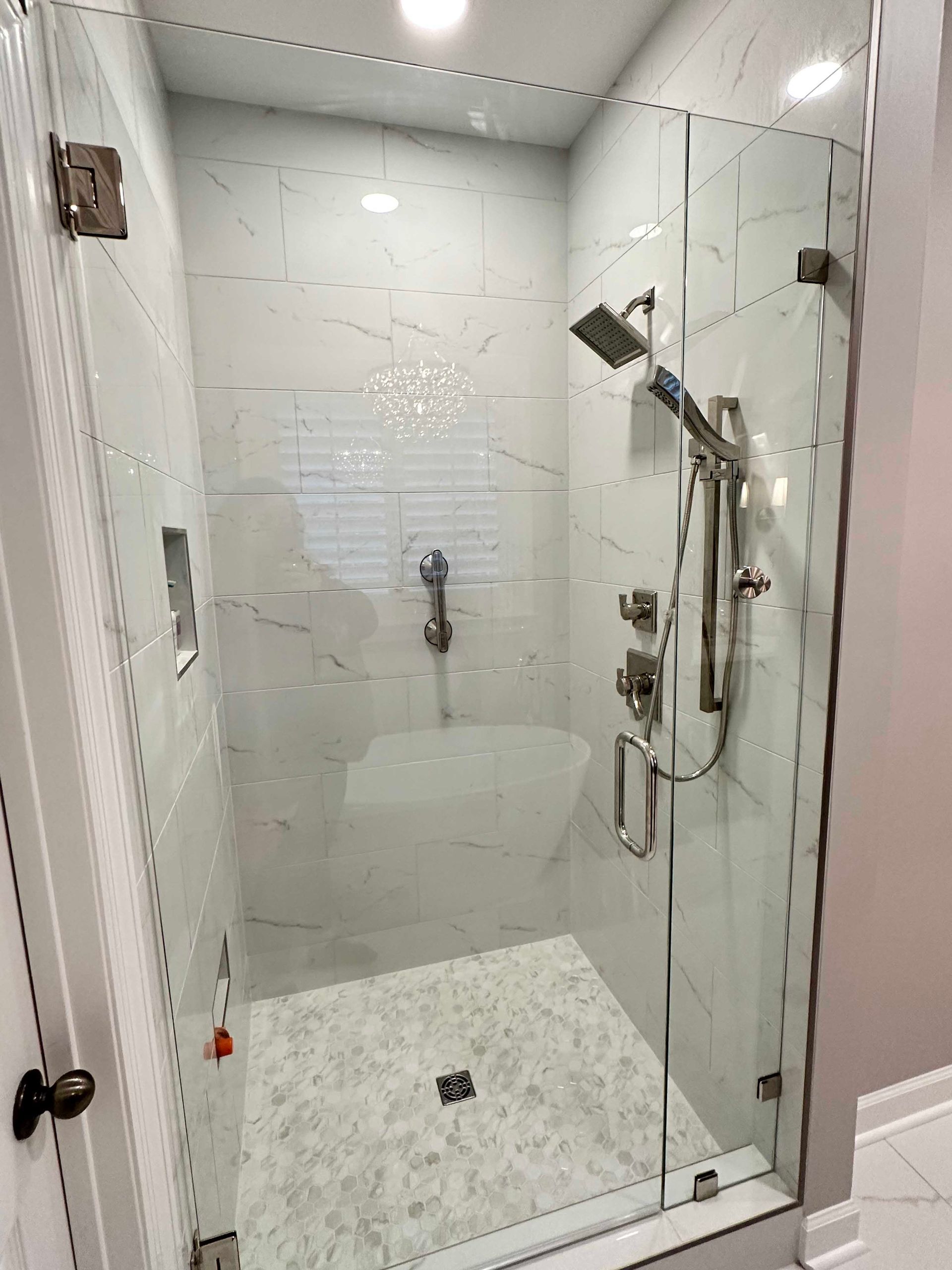 Glass shower with white marble-like tiles, silver fixtures.