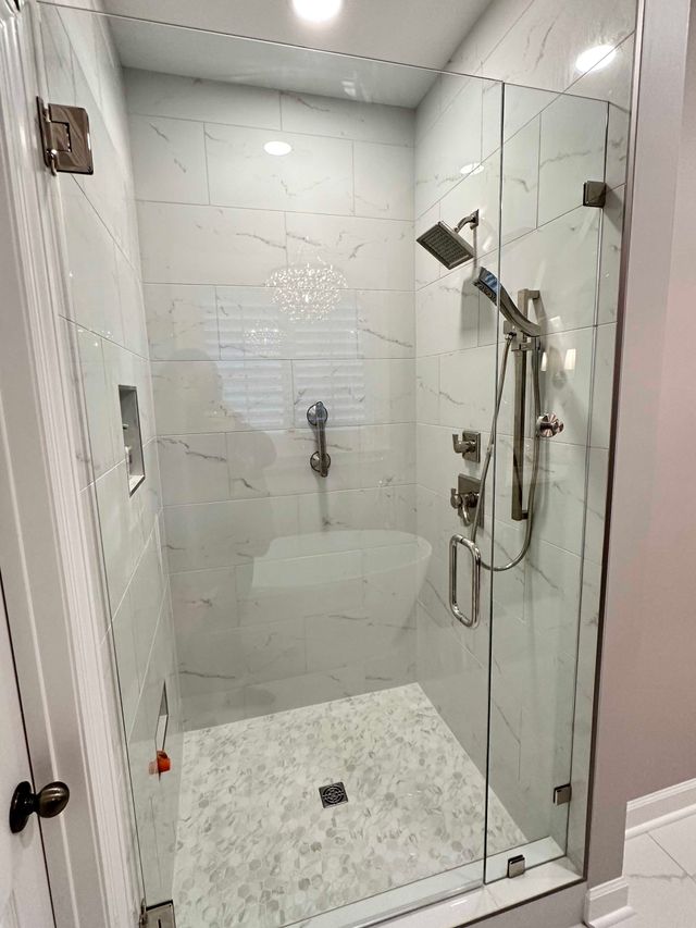 Glass shower with white marble-like tiles, silver fixtures.