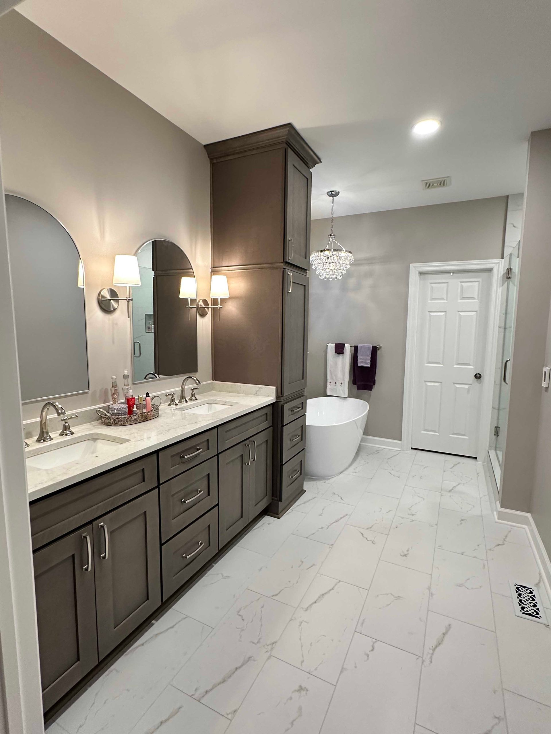 Gray and white bathroom with double vanity, tall storage cabinet, and soaking tub.