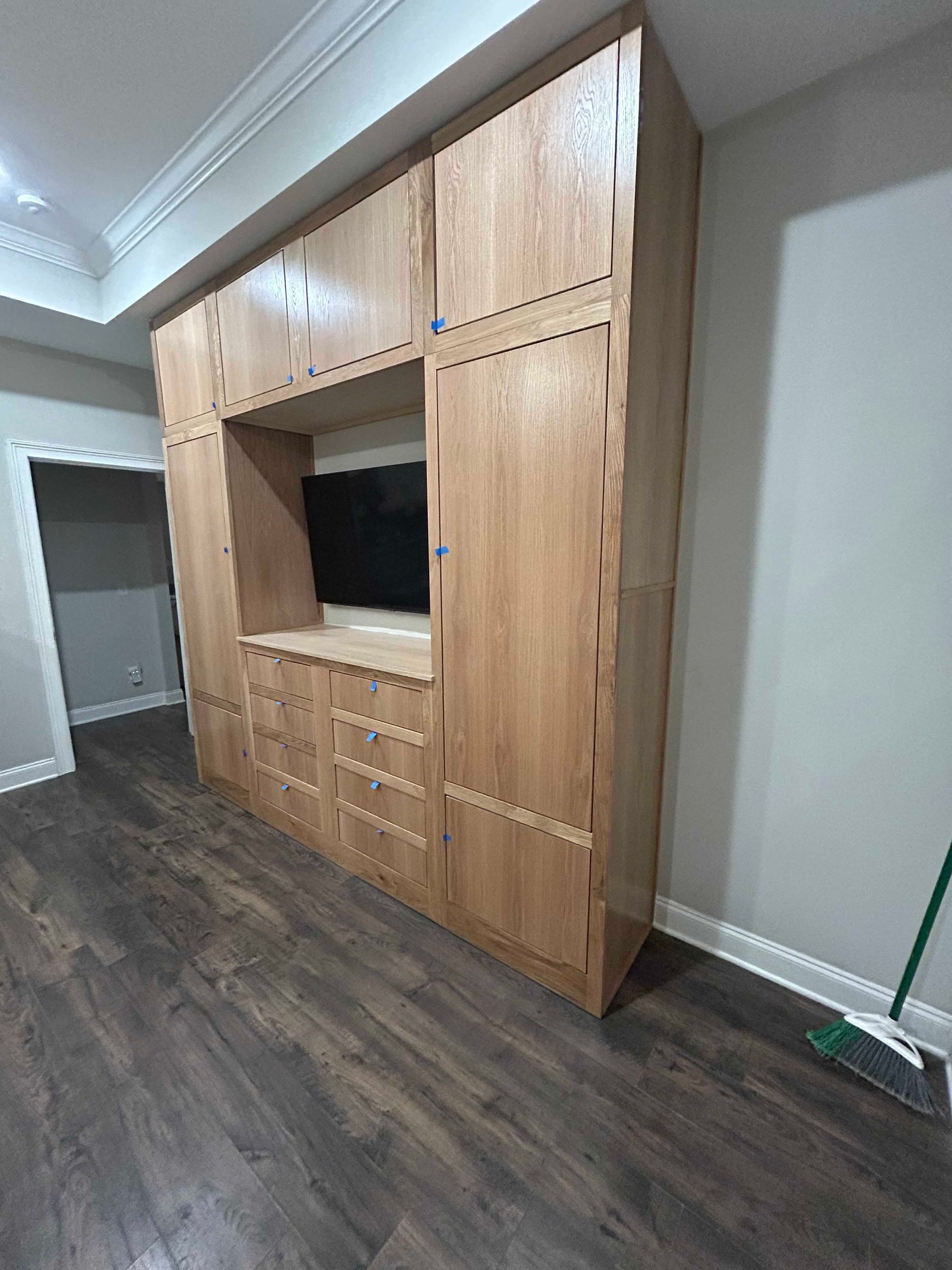 Wooden entertainment center with TV, drawers, and cabinets in a room with wood flooring.