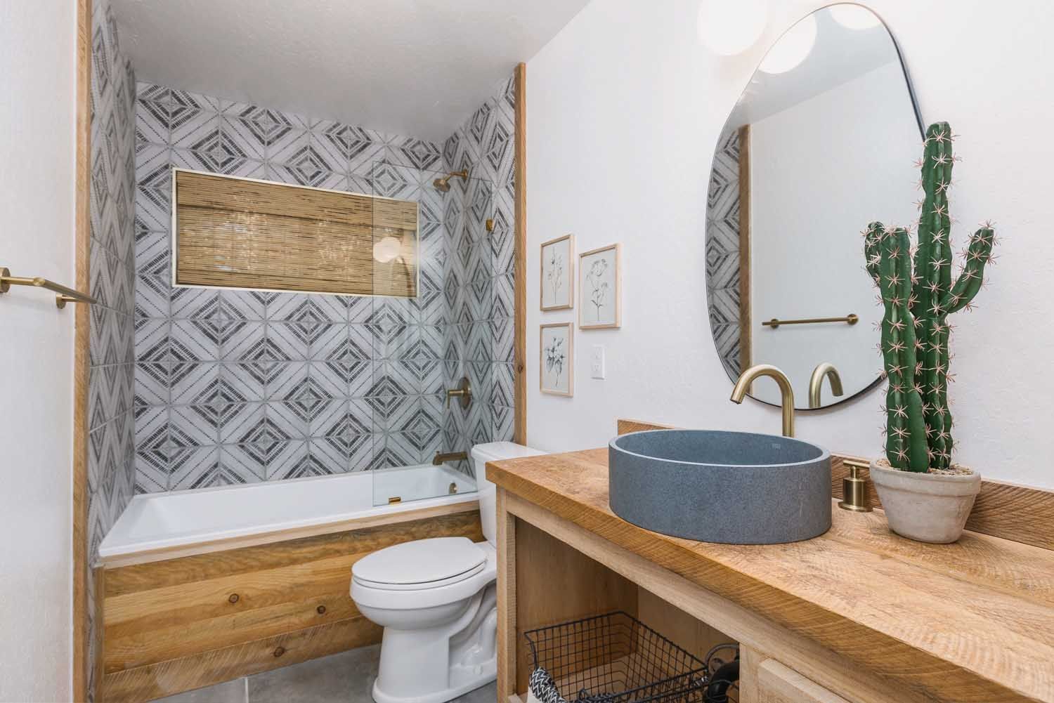 Bathroom with blue and white tile, wood accents, and a round mirror.
