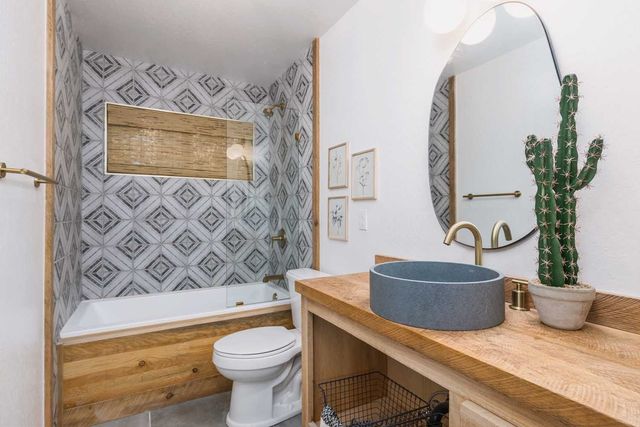 Bathroom with blue and white tile, wood accents, and a round mirror.