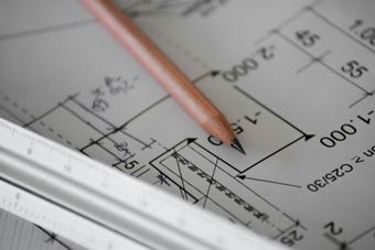A pencil is laying on top of a blueprint with a ruler next to it