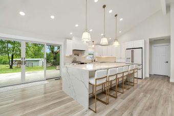A kitchen with white cabinets , a large island , and stools.