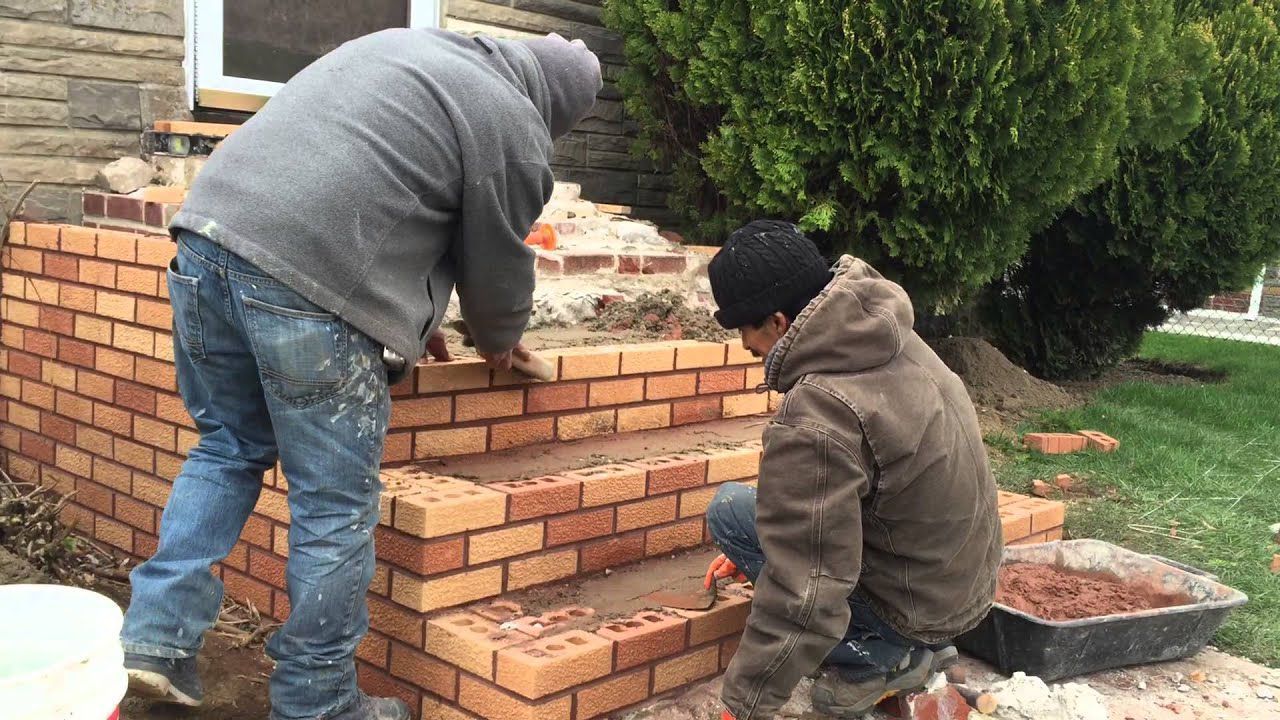 Two men are working on a brick wall in front of a house.