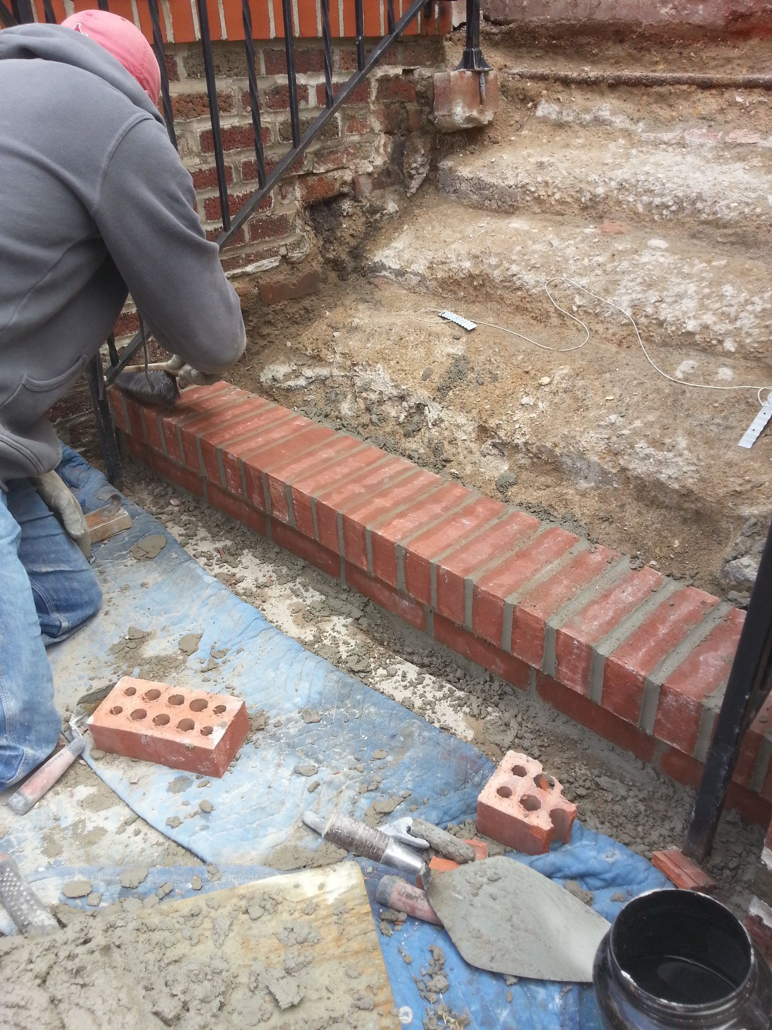 A man is kneeling down to build a brick wall.