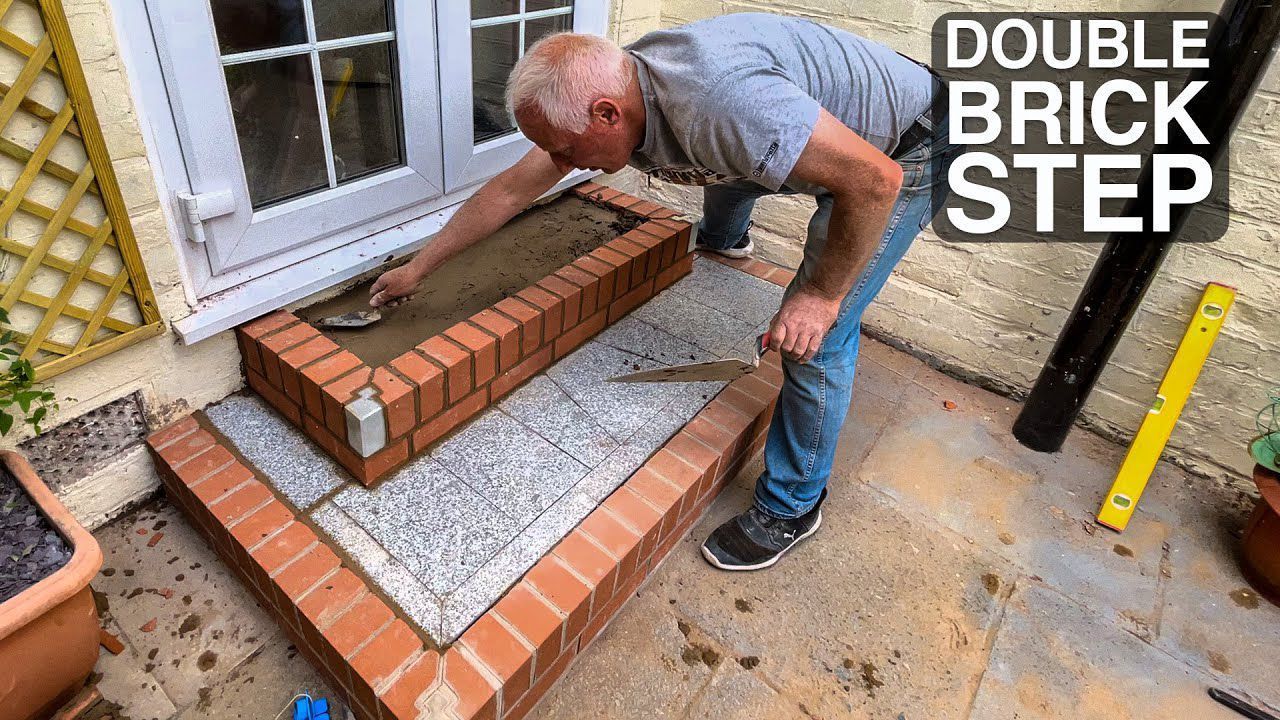 A man is laying bricks on a brick step.
