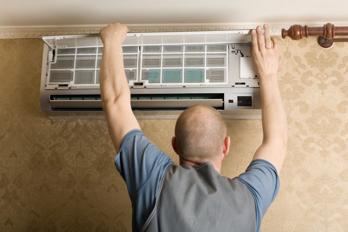 Man cleaning an air conditioner filter on a wall.