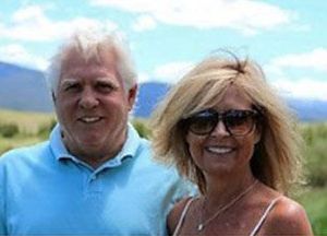 Man and woman smiling outdoors, man in blue shirt, woman wearing sunglasses.