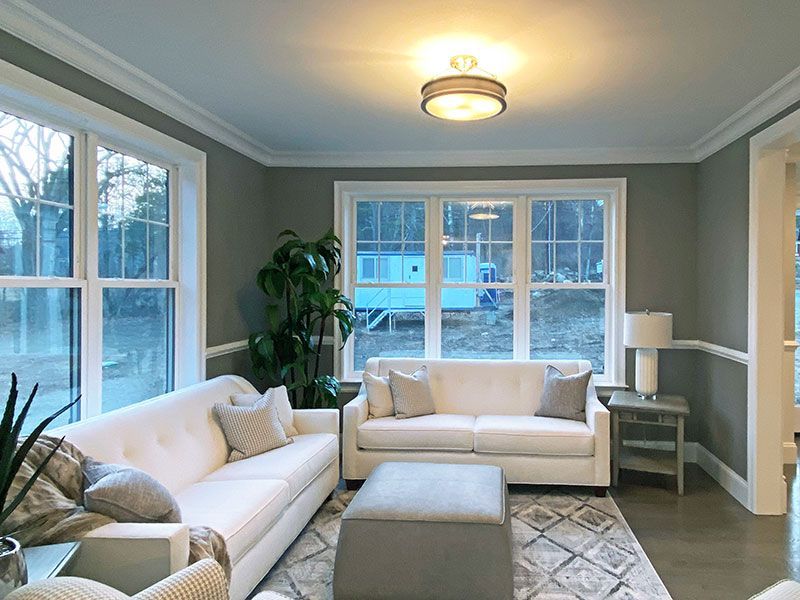 A living room with a white couch , ottoman , chairs , and windows.