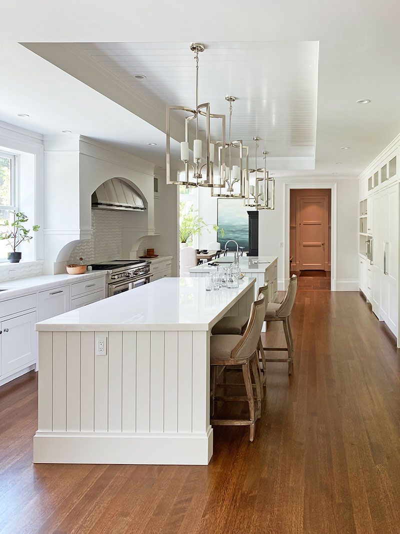 A kitchen with a long island , white cabinets , and wooden floors.