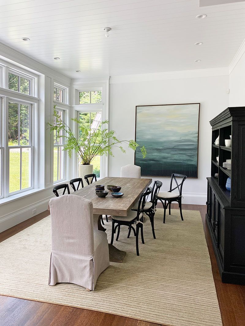 A dining room with a table and chairs and a painting on the wall.