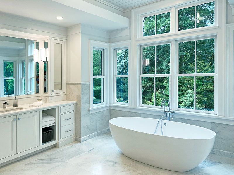 A bathroom with a tub , sink , mirror and lots of windows.