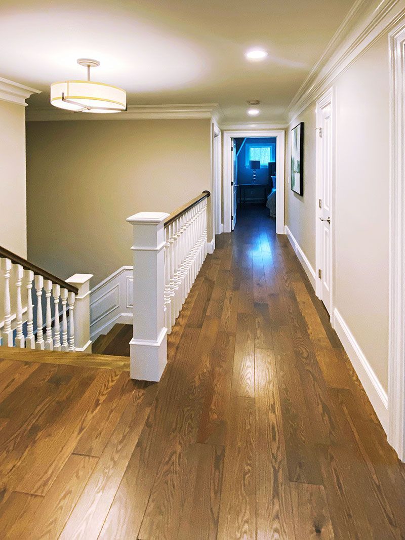 A long hallway with wooden floors and stairs in a house.