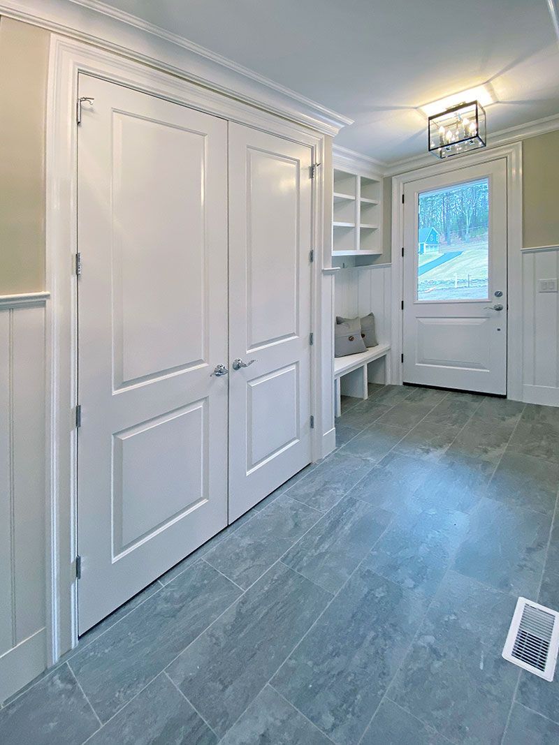 A hallway with white doors , a bench , and a window.