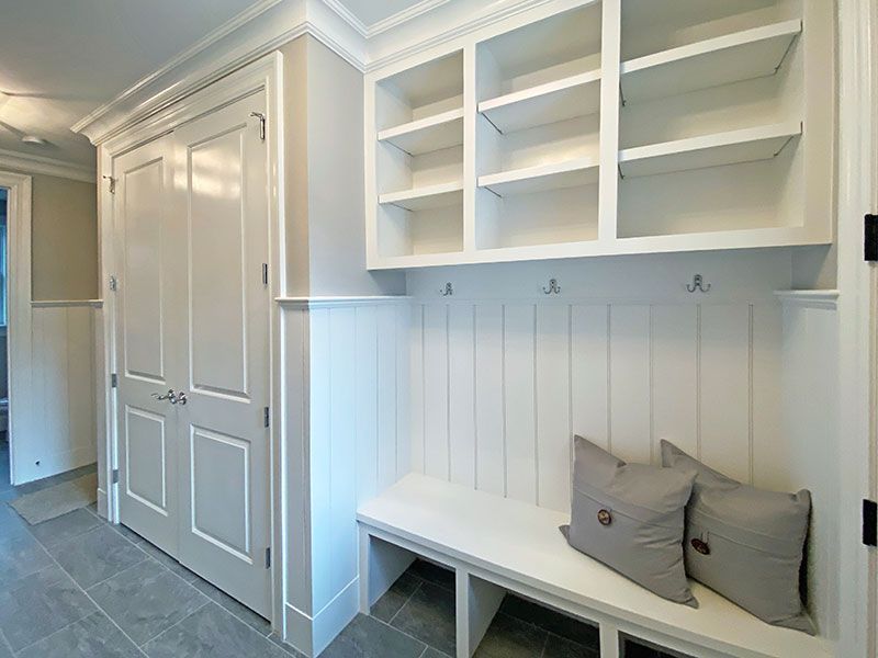 A mud room with a bench , shelves , hooks and pillows.
