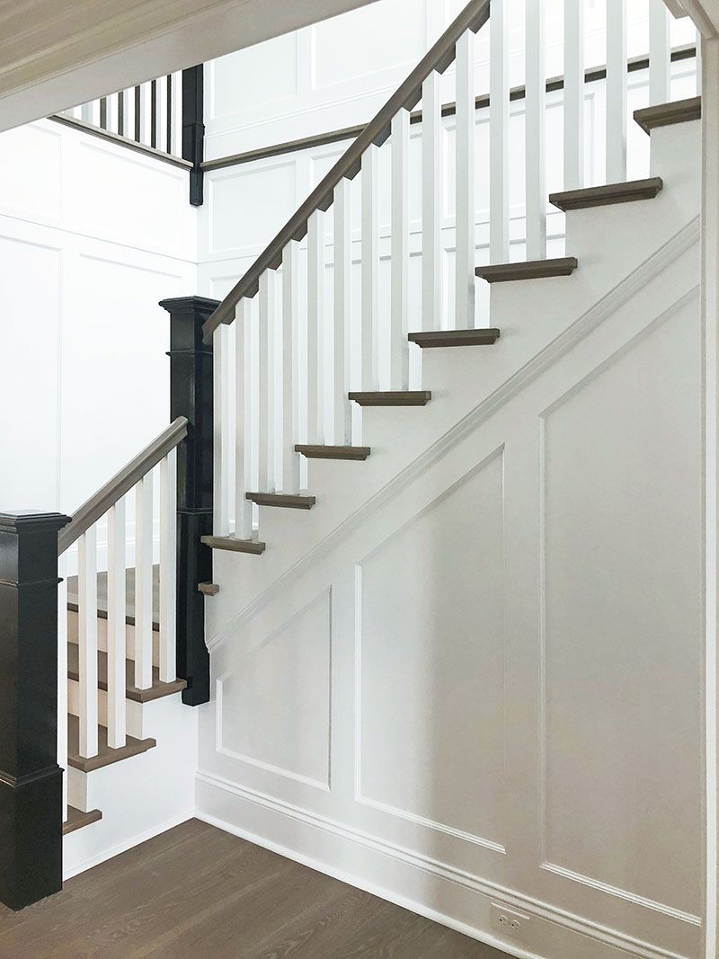 A white staircase with wooden steps and a black railing in a hallway.