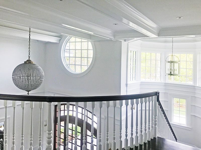 A staircase with a round window and a chandelier hanging from the ceiling.