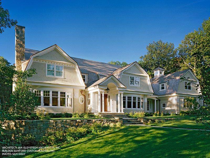A large white house with a gray roof is surrounded by trees and grass.