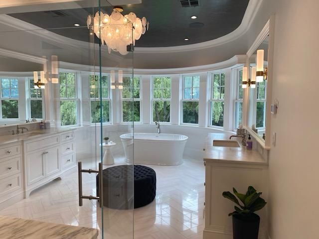 A bathroom with a tub , sinks , mirrors and a chandelier.