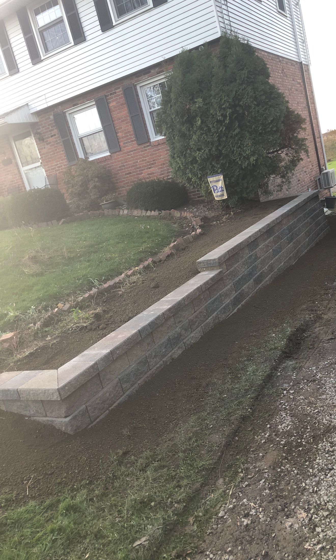 A brick house with a retaining wall and partially bare garden bed.