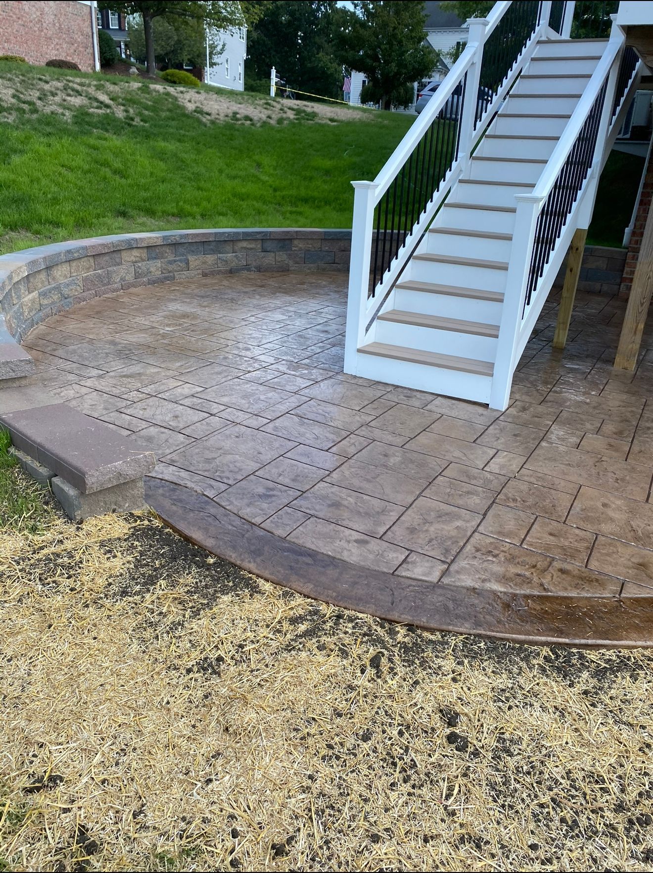 Patio with stone pavers and steps leading up. Brown retaining wall and stairs with white railings.