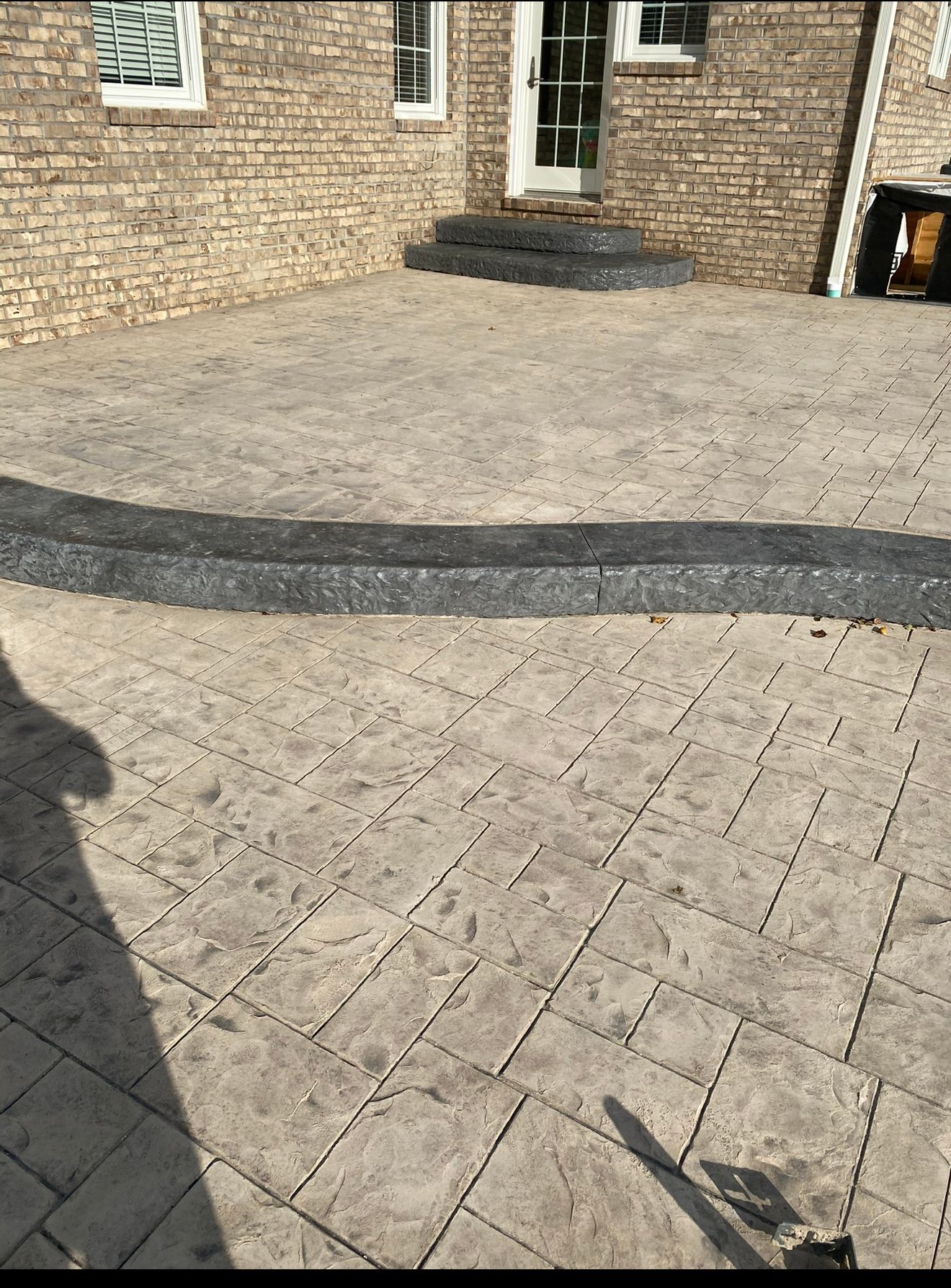 Stamped concrete patio with a dark border in front of a brick building.