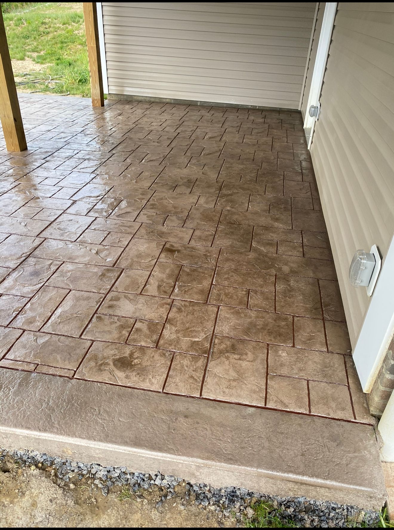Brown stamped concrete patio with a brick pattern. Next to a light beige house.